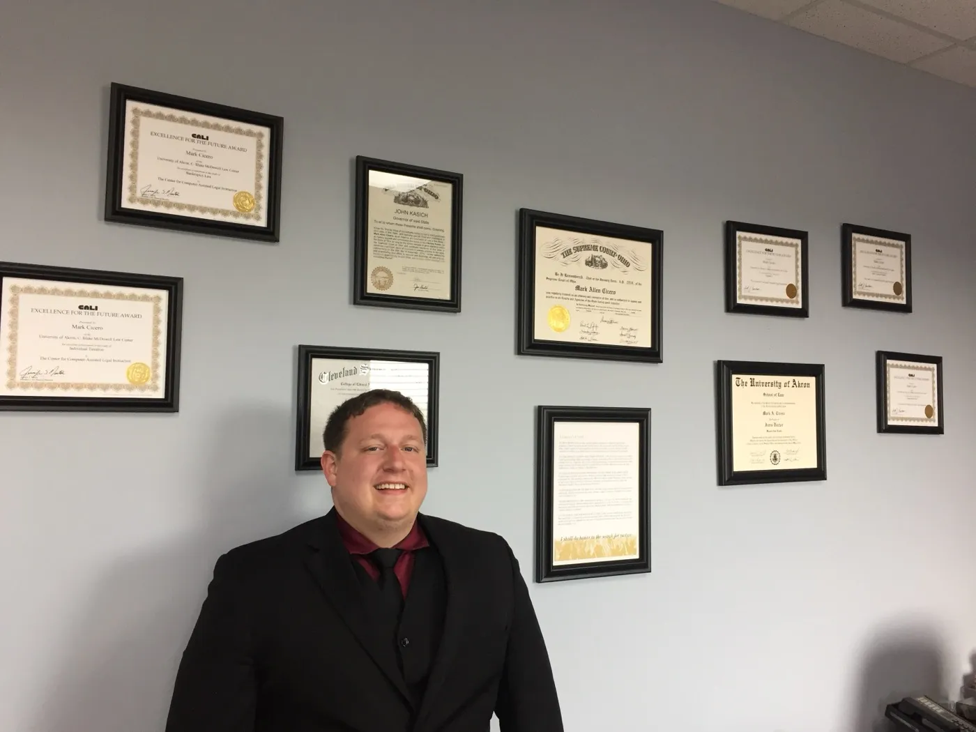 Mark Cicero seated before his framed diplomas and certificates